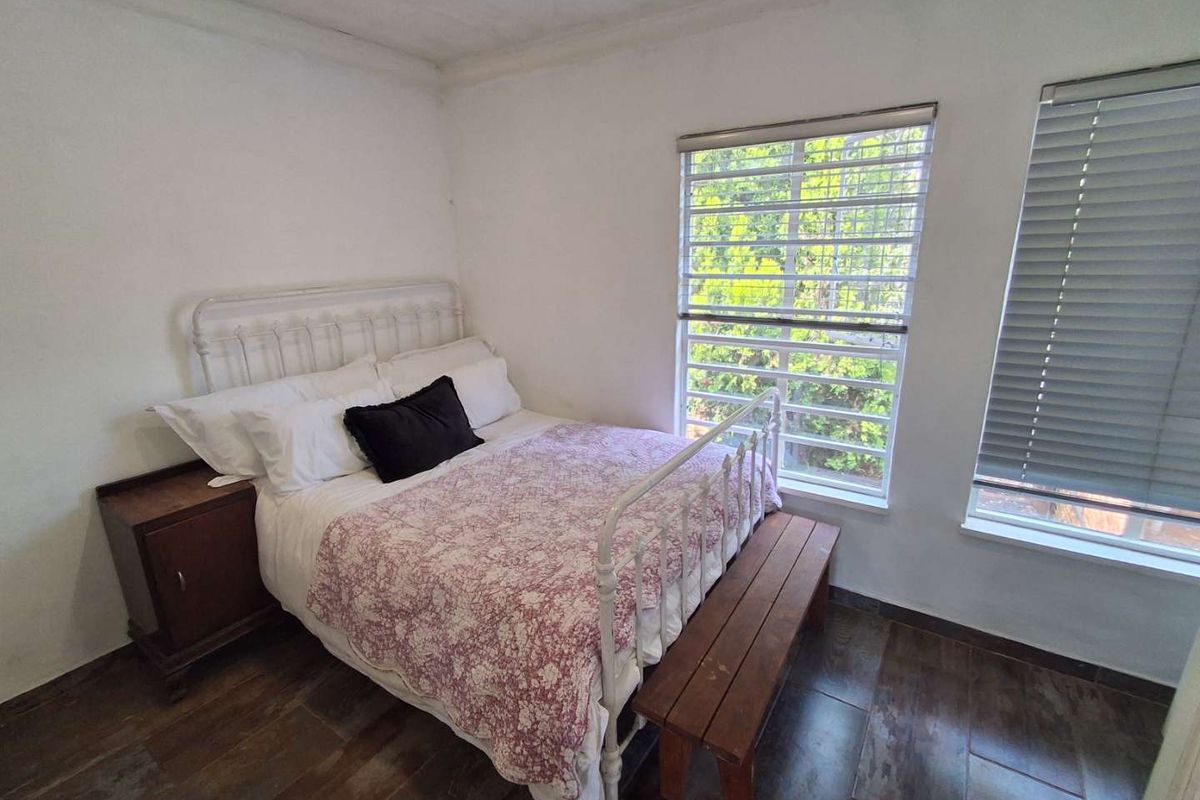 A bedroom featuring tiled flooring, large windows with fitted blinds, and security bars, providing natural light and a view of the surrounding greenery.