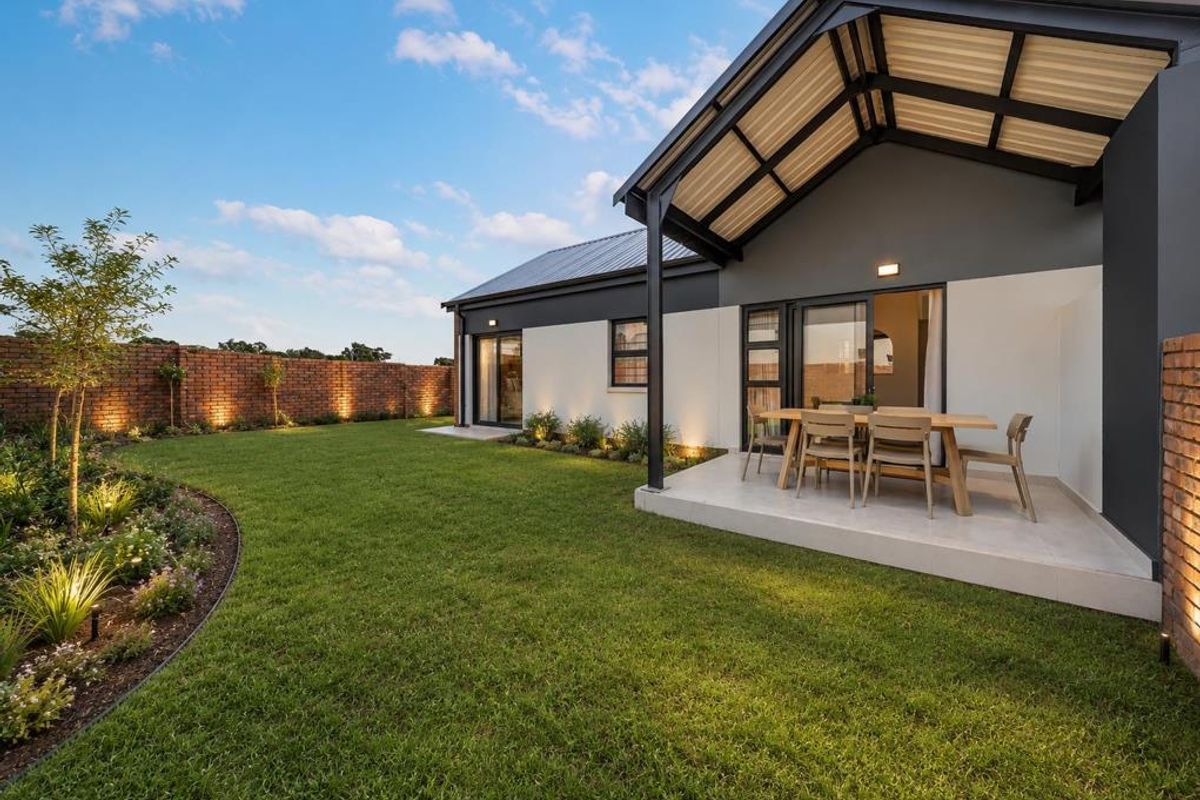 A well-maintained rear garden featuring a covered patio area, brick boundary walls with integrated lighting, and a neatly landscaped lawn.