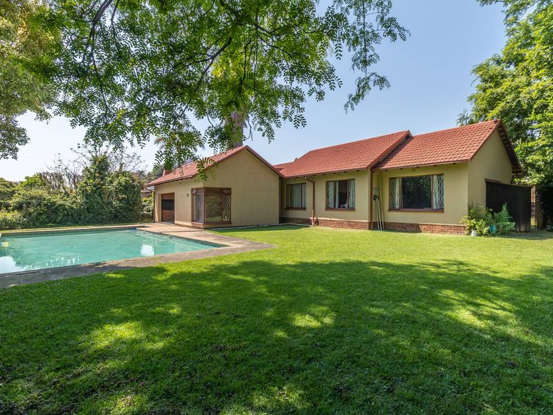 Rear view of the house featuring a spacious lawn, a swimming pool, and a traditional tiled roof structure.