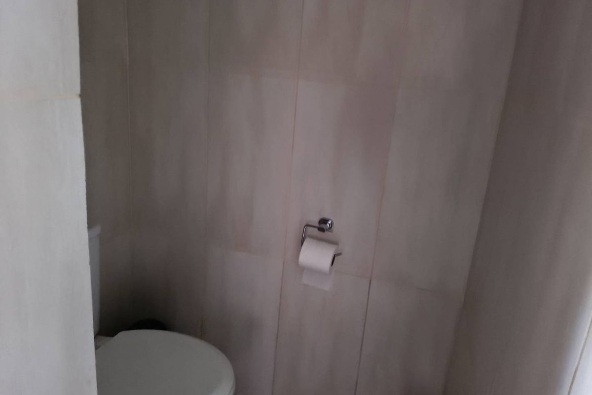 A compact bathroom featuring neutral wall tiling and a standard toilet fixture.