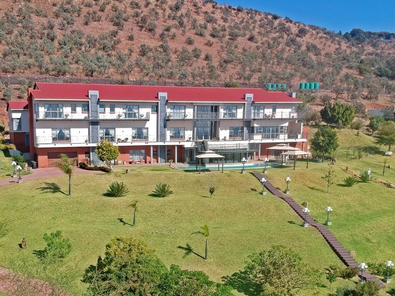 Aerial view of a large multi-story residence featuring a red roof, multiple balconies, a swimming pool, and extensive landscaped grounds set against a hillside.
