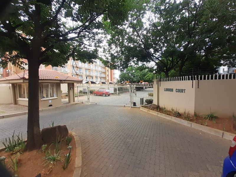 The entrance to Lunnon Court apartment complex featuring a secure gated access point, guard house, and paved driveway.