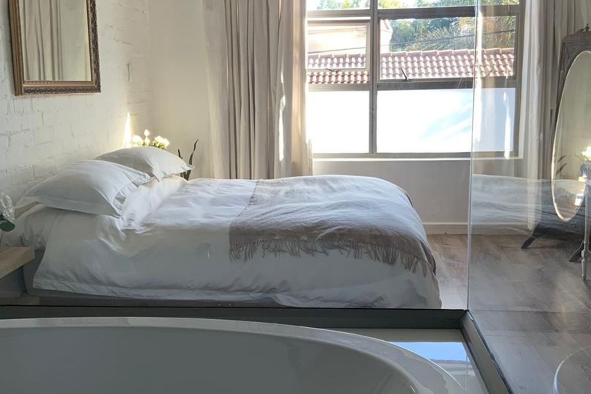 Modern bedroom featuring an open-plan design with an integrated freestanding bathtub, exposed brick wall, and large window providing ample natural light.