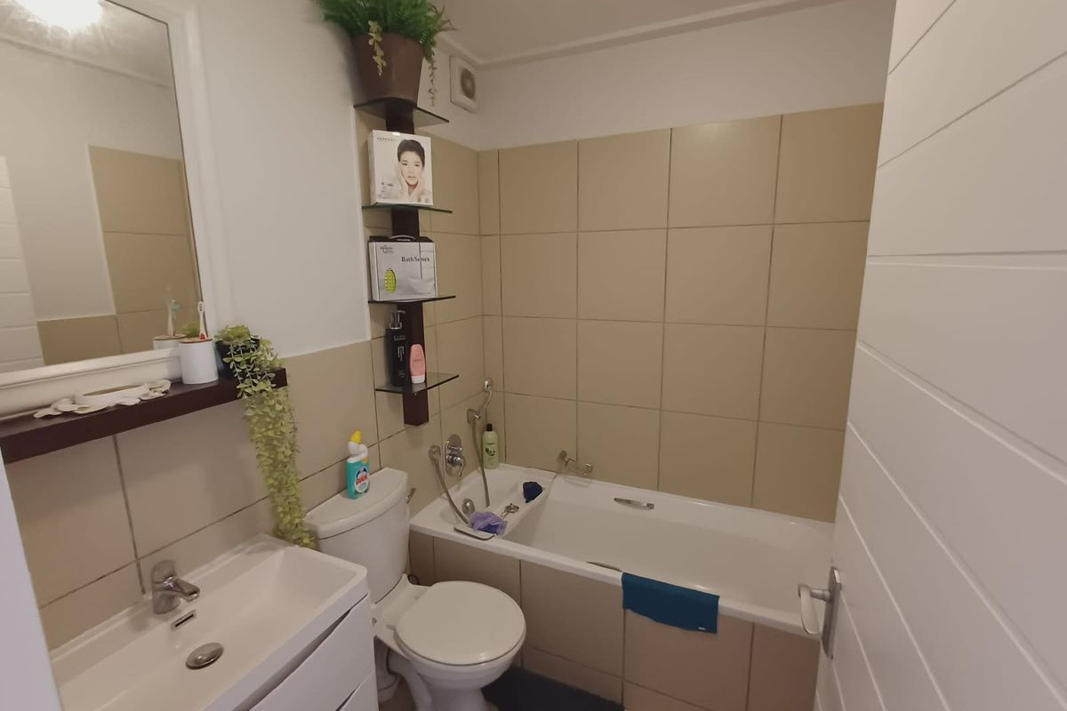 A functional bathroom featuring a bathtub, wall-mounted basin, toilet, and neutral wall tiling with integrated shelving.