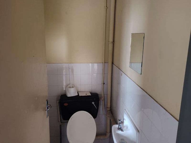 A compact, functional bathroom featuring a toilet, wall-mounted basin, and tiled splashback, currently in need of cosmetic updates and maintenance.