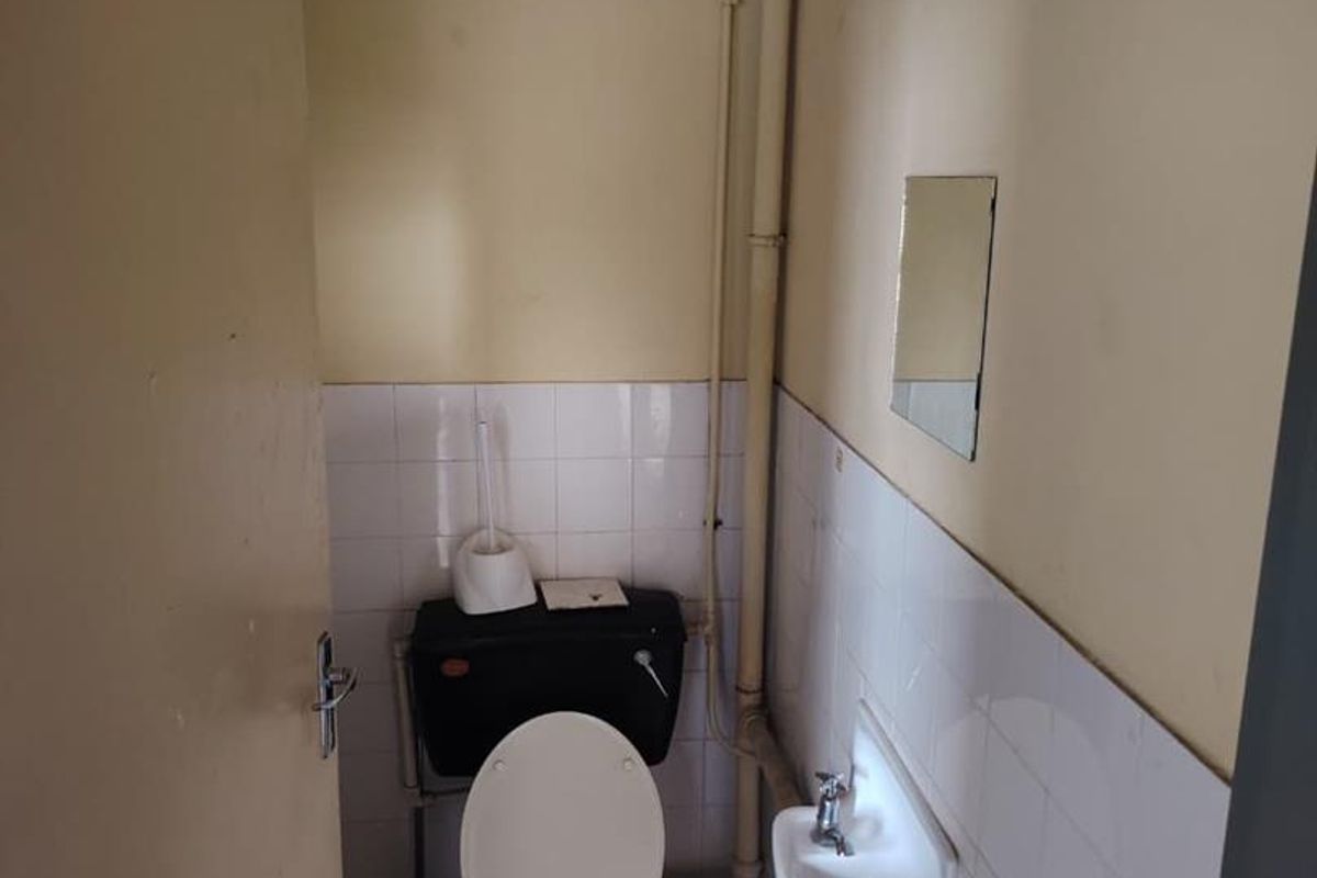 A compact, functional bathroom featuring a toilet, wall-mounted basin, and tiled splashback, currently in need of cosmetic updates and maintenance.