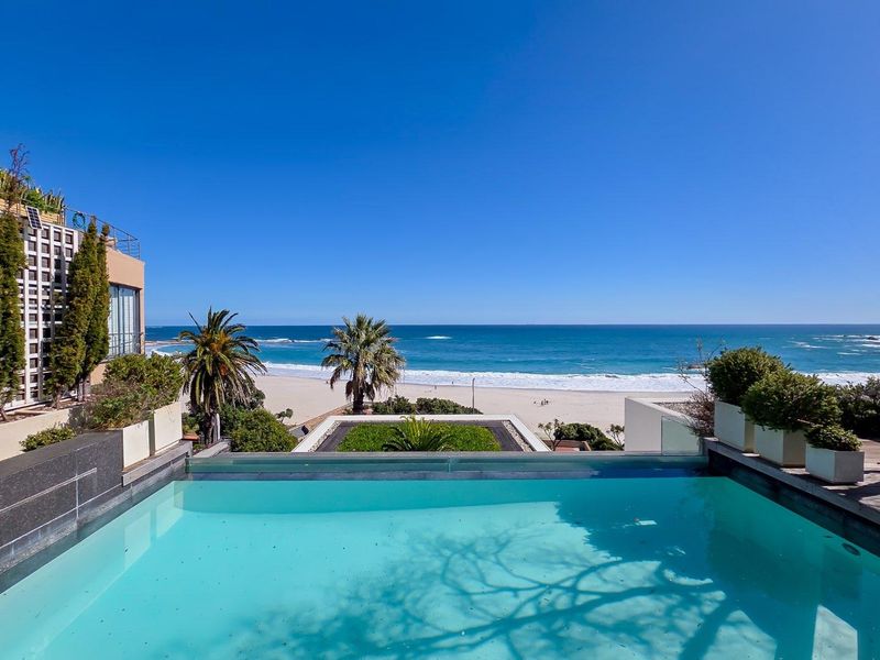 A stunning infinity edge swimming pool overlooking the ocean and beach, featuring a glass balustrade and integrated planters.