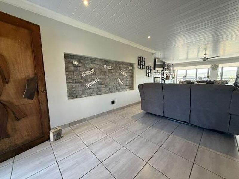Spacious living area featuring a stone-clad feature wall, tiled flooring, and a tongue and groove ceiling with recessed lighting.