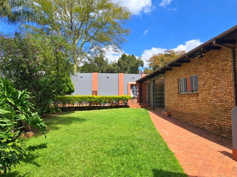 A well-maintained rear garden featuring a brick-paved walkway, lush lawn, and established landscaping alongside the face brick exterior of the house.