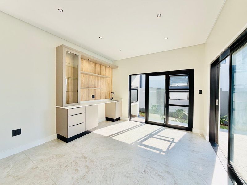 Bright living area featuring modern built-in cabinetry with integrated shelving, a sink, tiled flooring, and large sliding glass doors leading to the exterior.