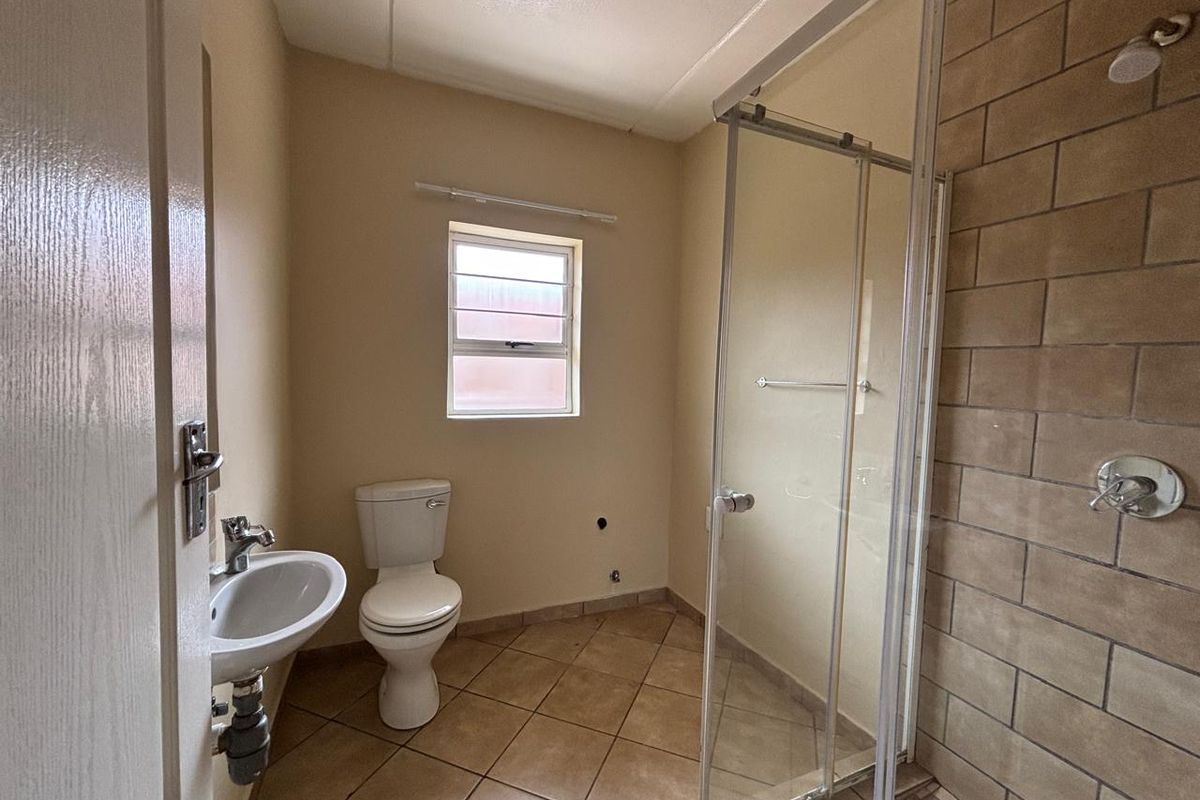 A functional bathroom featuring a tiled shower enclosure, pedestal basin, and toilet with neutral wall finishes and tiled flooring.