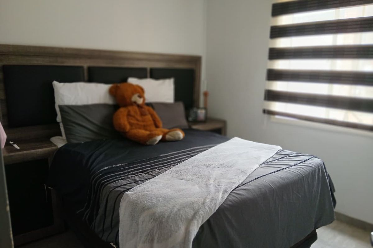 A well-maintained bedroom featuring a built-in headboard with integrated side tables and modern zebra-style window blinds.