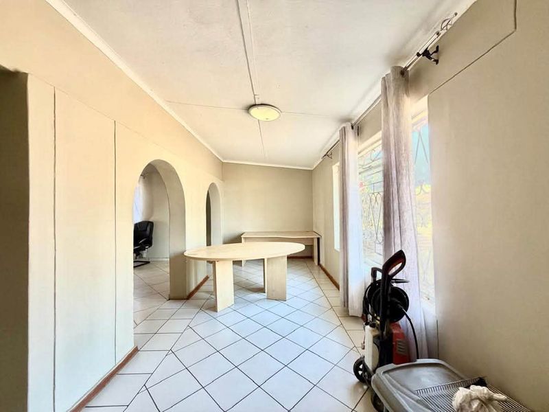 A functional office space featuring tiled flooring, arched architectural details, and large windows with security bars, offering a bright and versatile work environment.