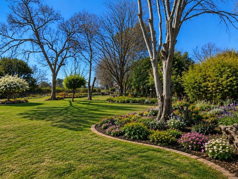A beautifully maintained, expansive garden featuring mature trees, lush green lawn, and vibrant flower beds with neat brick edging.