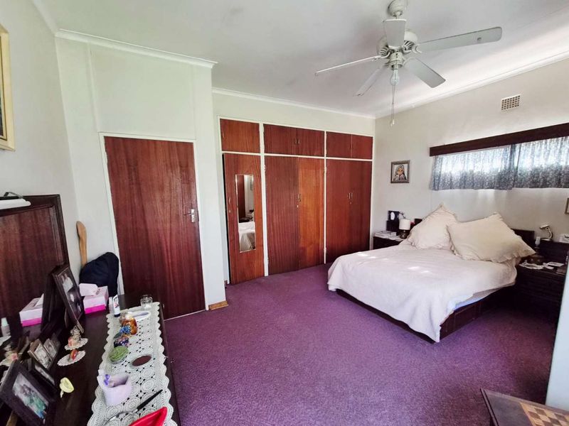 Spacious bedroom featuring extensive built-in wooden cupboards, a ceiling fan, and neutral wall finishes, offering a functional layout with potential for modern updates.