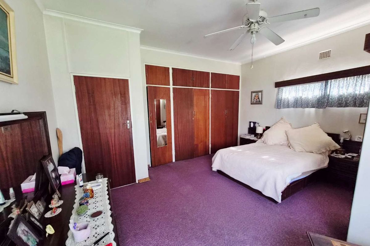 Spacious bedroom featuring extensive built-in wooden cupboards, a ceiling fan, and neutral wall finishes, offering a functional layout with potential for modern updates.