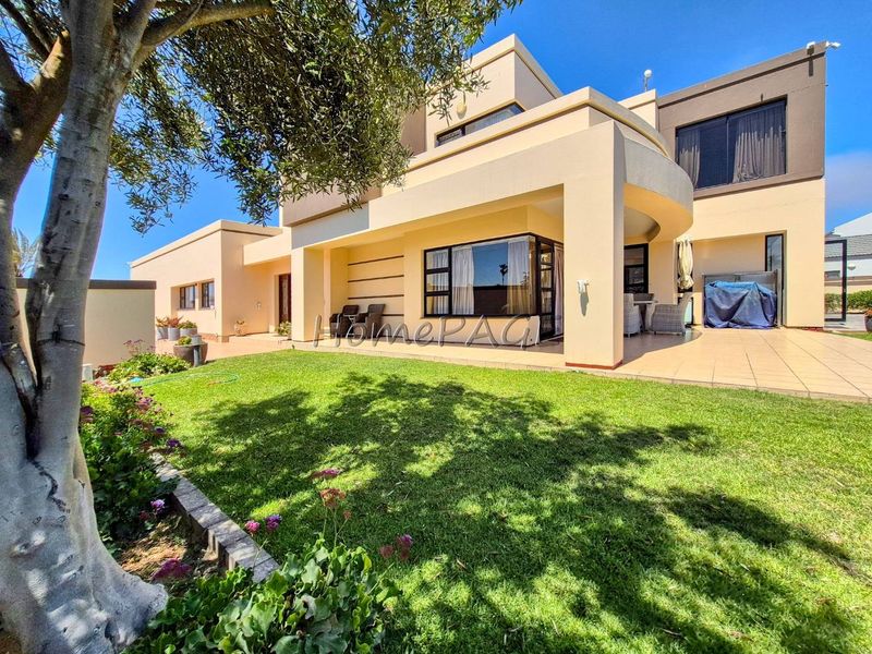 A well-maintained rear exterior view featuring a spacious tiled patio, landscaped garden, and modern stucco facade with large sliding glass doors.