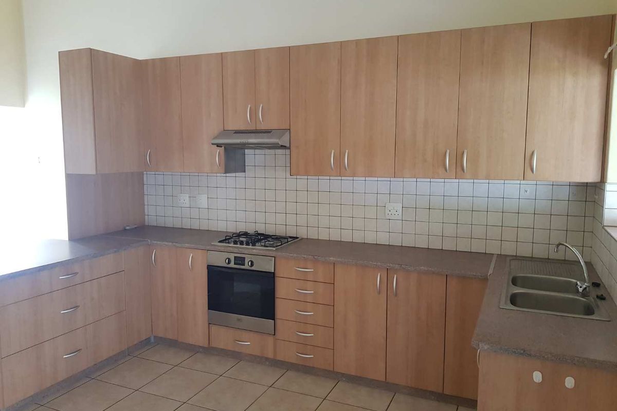 Functional kitchen featuring light wood-finish cabinetry, tiled backsplash, built-in oven, gas hob, extractor fan, and a double-basin stainless steel sink.