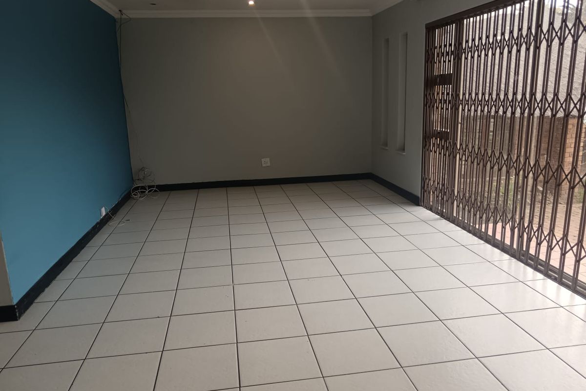 An empty living room featuring tiled flooring, a blue accent wall, and a large sliding door secured with a metal security gate.