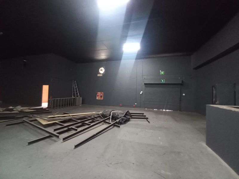 Spacious industrial utility area featuring a roller shutter door, industrial ventilation, and emergency exit access, suitable for storage or workshop operations.