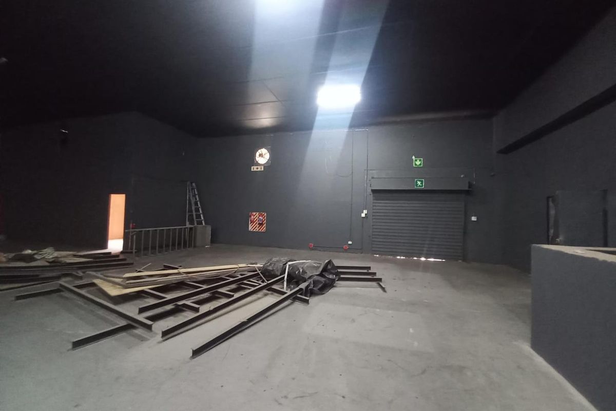 Spacious industrial utility area featuring a roller shutter door, industrial ventilation, and emergency exit access, suitable for storage or workshop operations.