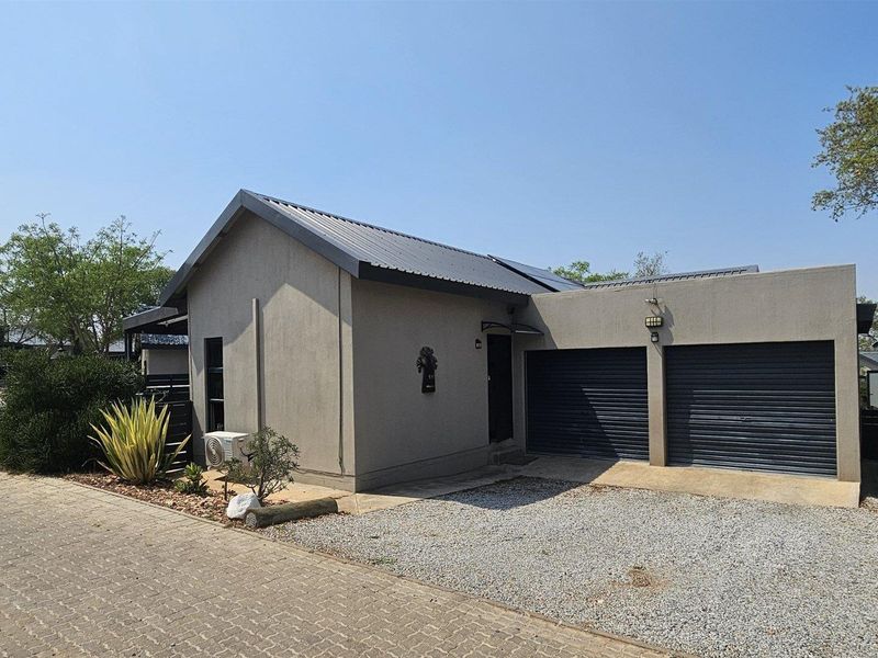 Front view of a modern house featuring a double garage, metal roofing with solar panels, and a paved driveway.