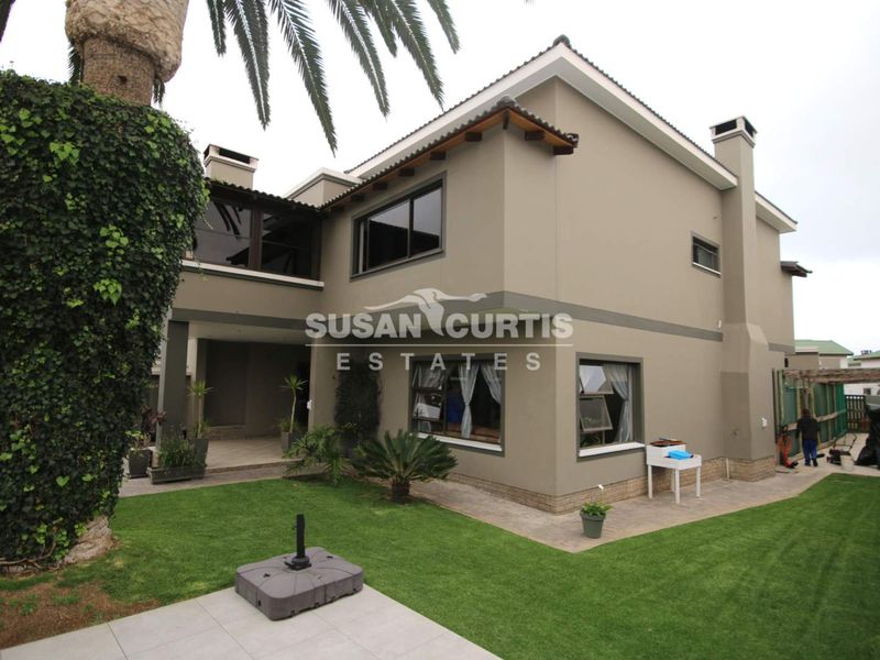 Rear view of a double-storey house featuring a covered patio, paved walkways, and a well-maintained lawn.
