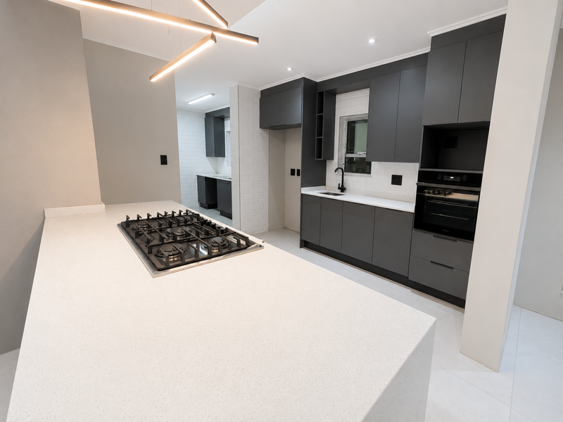 Modern kitchen featuring dark cabinetry, quartz countertops, a central island with a gas hob, and a separate scullery area with matching finishes.