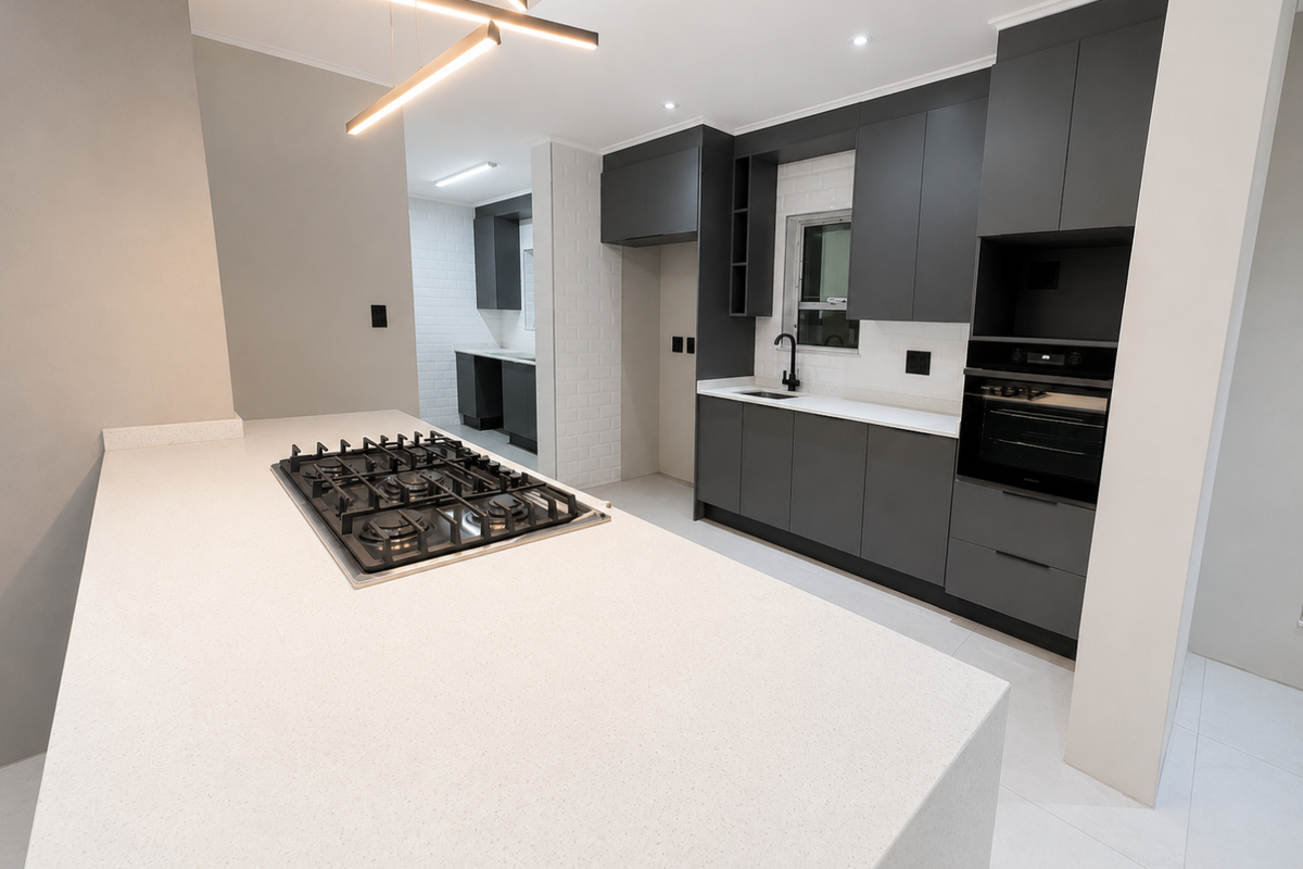 Modern kitchen featuring dark cabinetry, quartz countertops, a central island with a gas hob, and a separate scullery area with matching finishes.