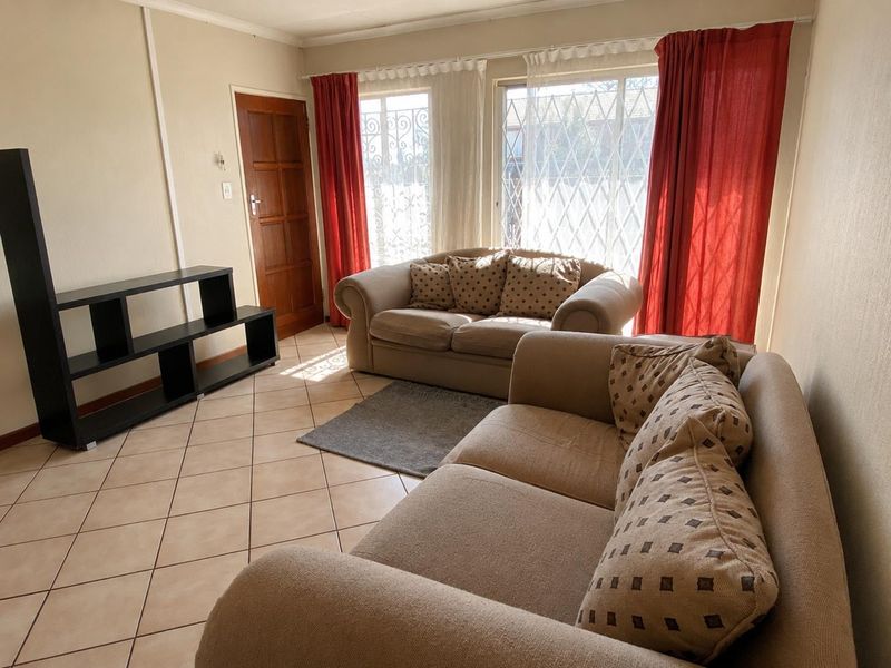A living room featuring ceramic floor tiles, a timber entrance door, and large windows fitted with security gates.