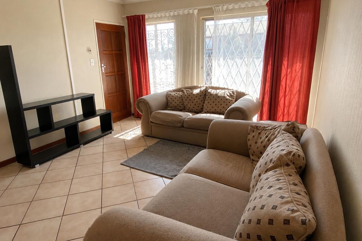 A living room featuring ceramic floor tiles, a timber entrance door, and large windows fitted with security gates.