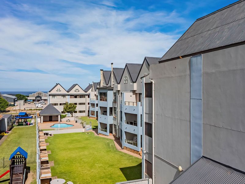 An aerial view of the apartment complex featuring a communal swimming pool, landscaped garden areas, and multi-story residential buildings with metal roofing.