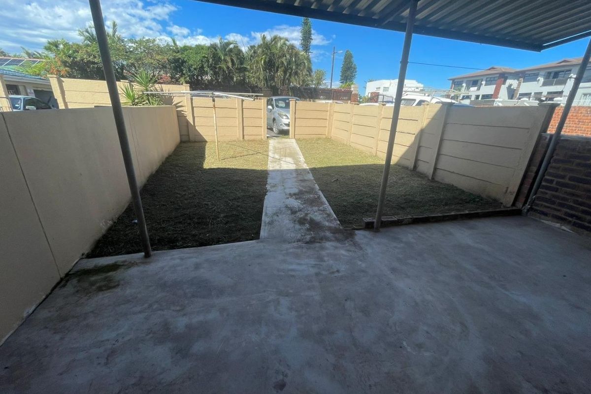 A private rear courtyard featuring a covered concrete patio, a central walkway, and a small lawn enclosed by precast concrete boundary walls.