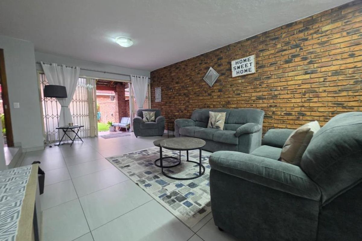 Spacious living room featuring a prominent exposed brick feature wall, large format floor tiles, and sliding glass doors leading to an outdoor patio area.