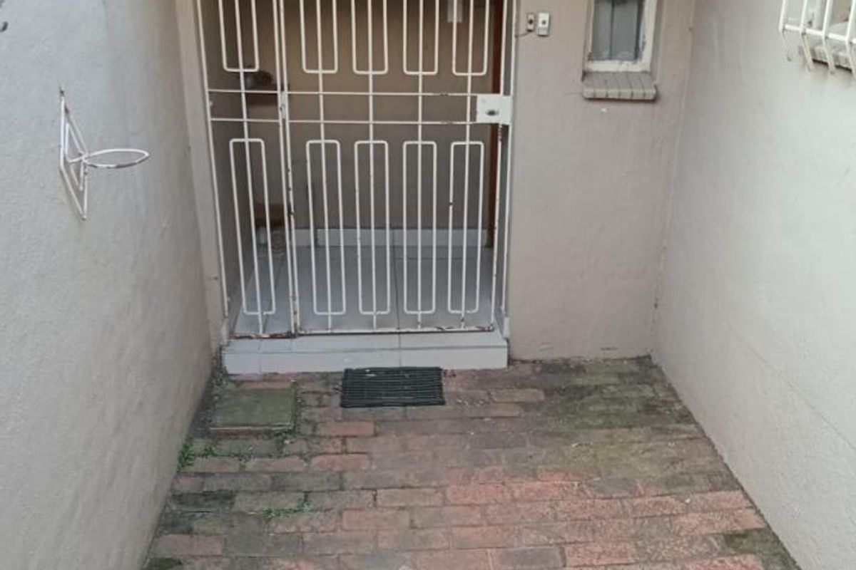 A small, paved rear courtyard area featuring a security gate entrance, brick flooring, and a protective awning over the doorway.