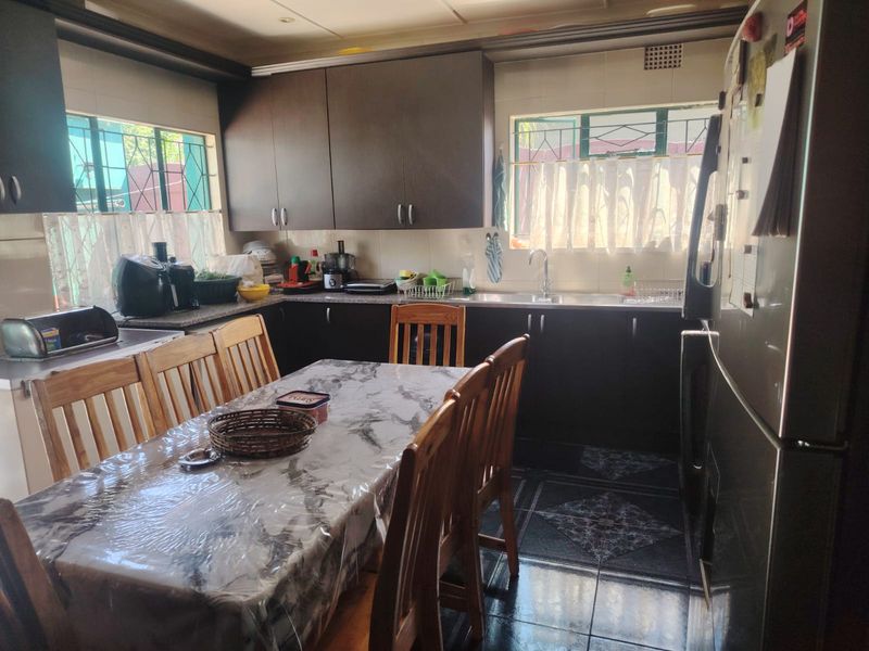 Open plan kitchen and dining area featuring dark cabinetry, tiled flooring, and functional workspace with integrated sink and security bars on windows.