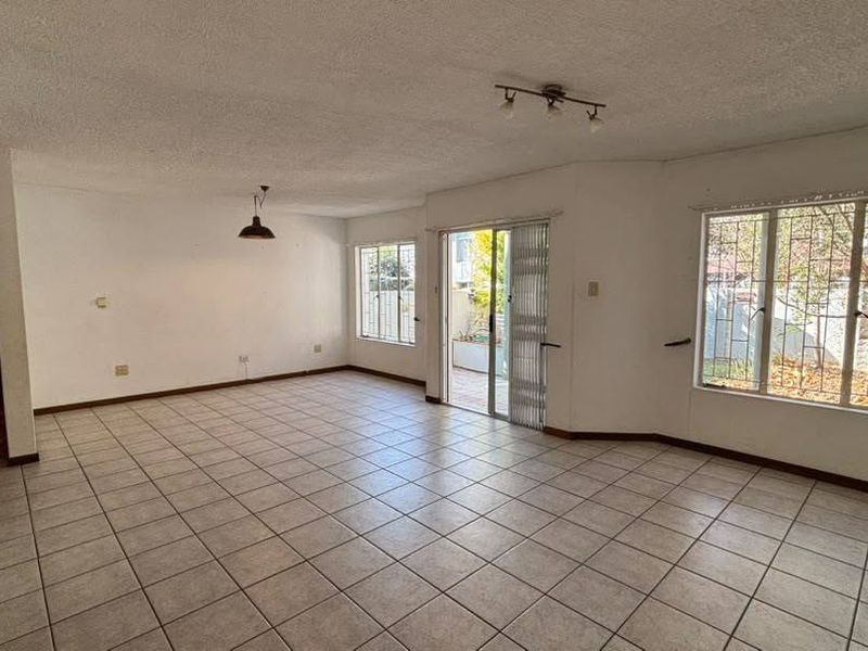 Spacious open-plan living area featuring ceramic tiled flooring, large windows with security bars, and a sliding glass door leading to the outdoor space.
