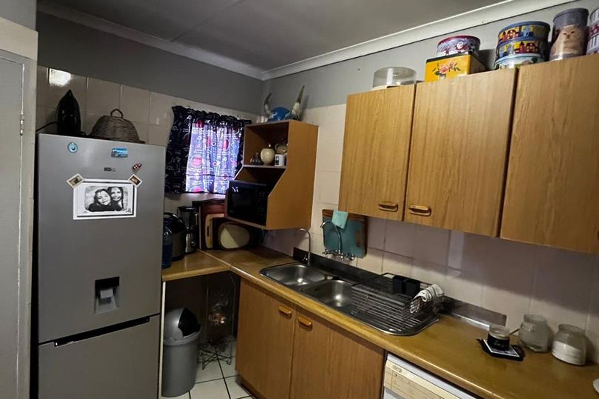 A functional kitchen featuring wood-look cabinetry, a double-basin sink, tiled flooring, and space for a washing machine.
