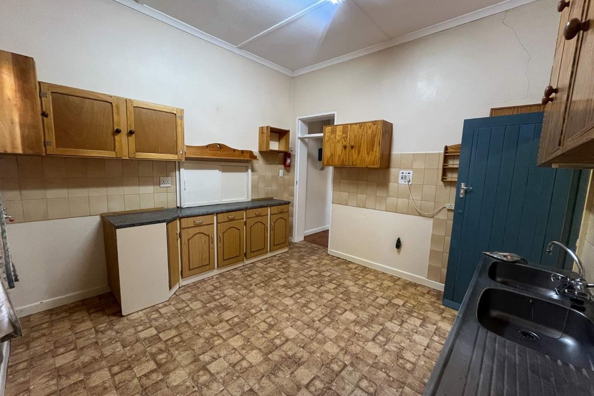 A dated kitchen featuring wooden cabinetry, tiled splashbacks, a double sink, and vinyl flooring, offering a functional space ready for modernization.