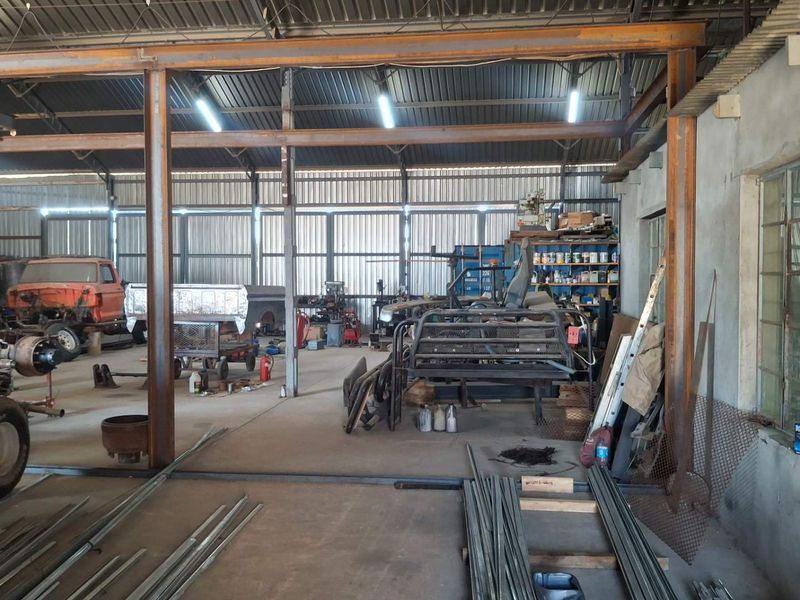 Spacious industrial workshop featuring a steel portal frame structure, corrugated metal walls, and concrete flooring, suitable for heavy-duty manufacturing or storage operations.