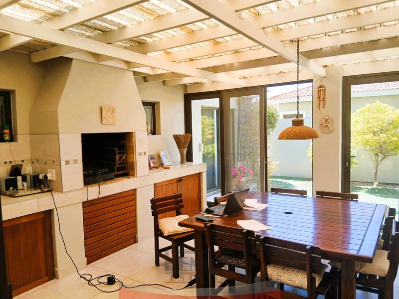 Covered patio area featuring a built-in braai, tiled flooring, and a timber pergola roof, providing a functional space for outdoor dining and entertainment.