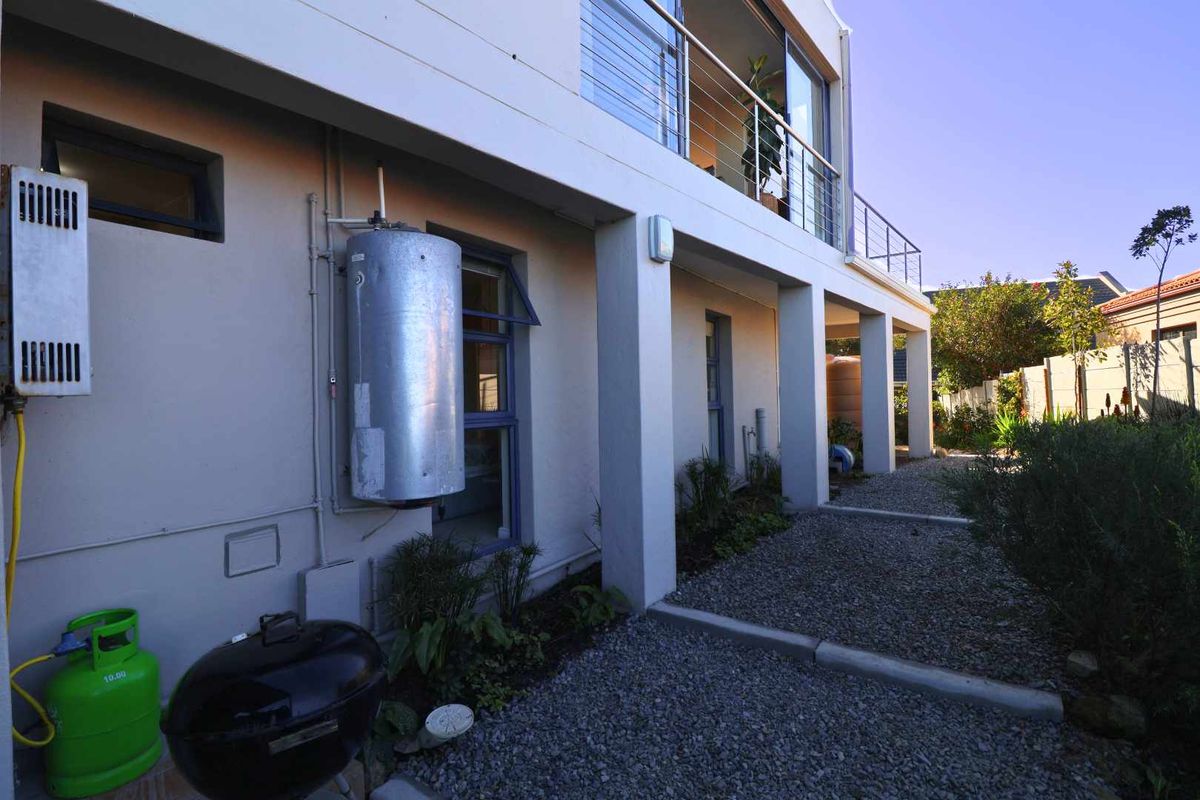 Rear exterior view of the property featuring a covered patio area, gravel landscaping, and external water heating infrastructure.