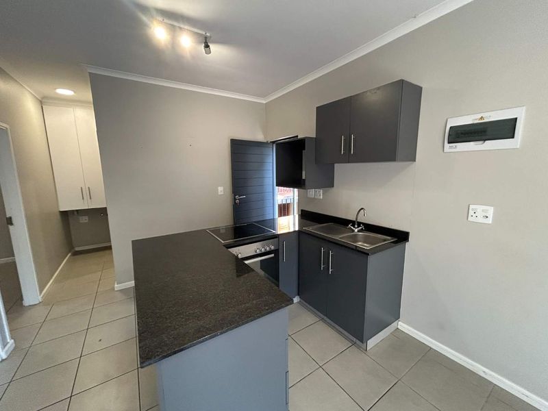 Modern kitchen featuring dark grey cabinetry, granite countertops, built-in oven, electric hob, and tiled flooring in an open-plan layout.