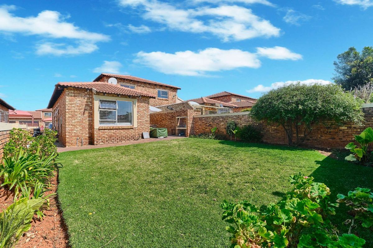 A well-maintained rear garden featuring a lush lawn, established perimeter brick boundary walls, and a classic face brick townhouse exterior.
