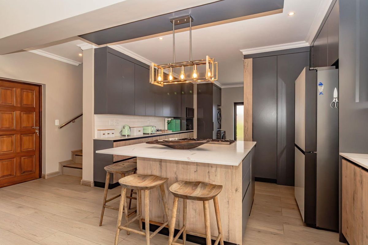 Modern open-plan kitchen featuring dark cabinetry, a central island with stone countertop, wood-look flooring, and contemporary pendant lighting.