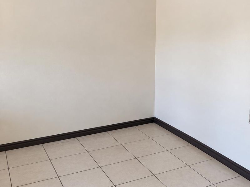 A clean, empty living area featuring neutral tiled flooring, dark skirting boards, and simple ceiling cornicing, providing a blank canvas for interior design.