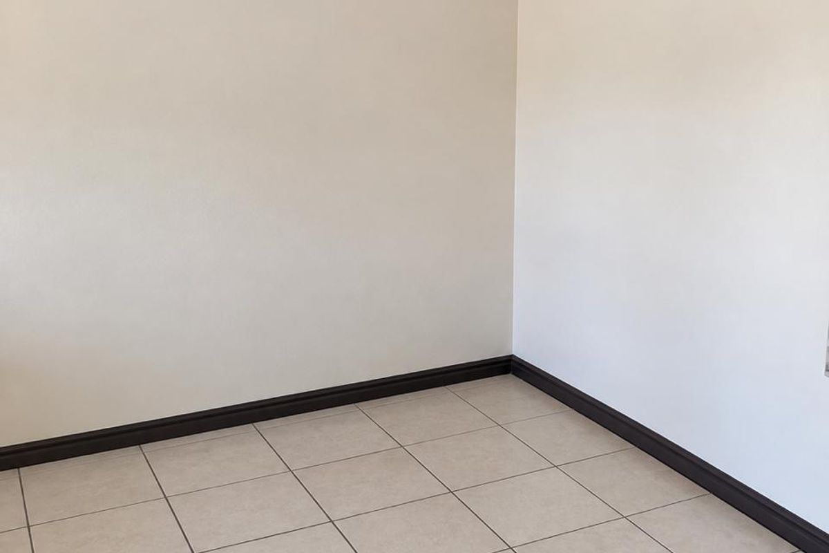 A clean, empty living area featuring neutral tiled flooring, dark skirting boards, and simple ceiling cornicing, providing a blank canvas for interior design.