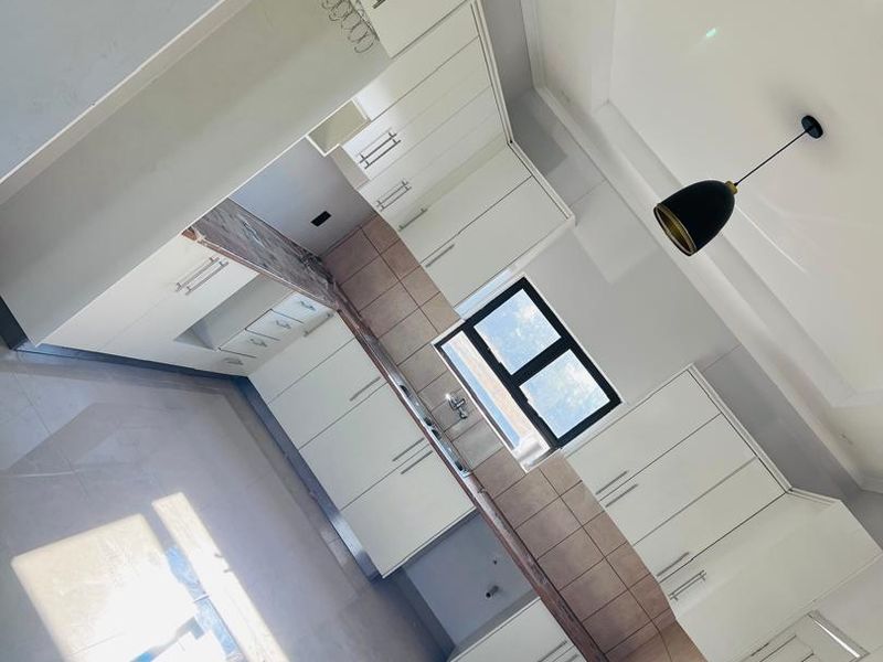 Modern, clean-lined kitchen featuring white cabinetry, stone countertops, tiled backsplash, and contemporary pendant lighting in a bright, open-plan layout.