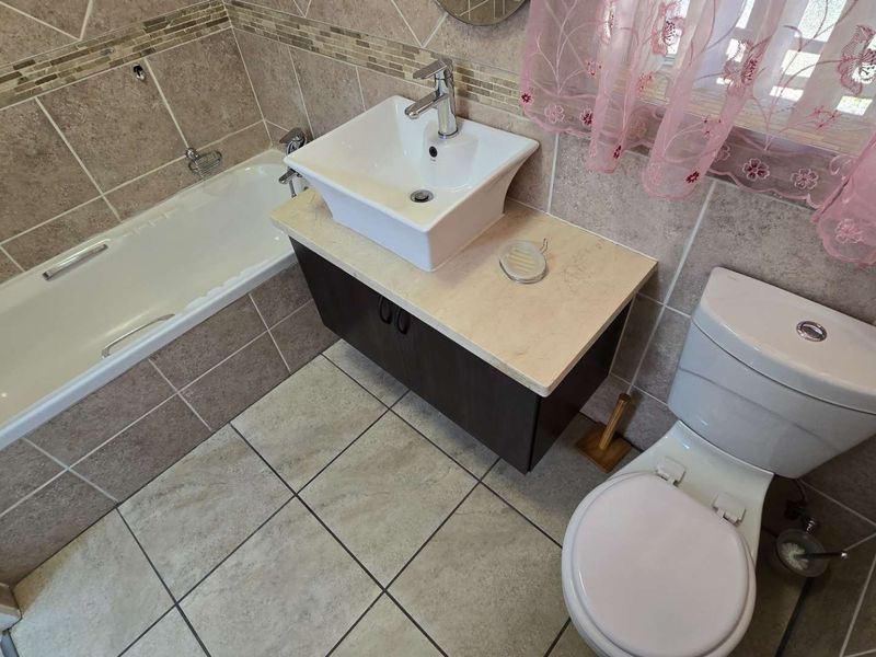 A functional bathroom featuring a bathtub, a modern vessel sink on a vanity cabinet, and a standard toilet with neutral wall and floor tiling.