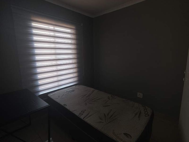 A bedroom featuring tiled flooring, roller blinds, and a ceiling light fixture, providing a functional space with neutral wall tones.